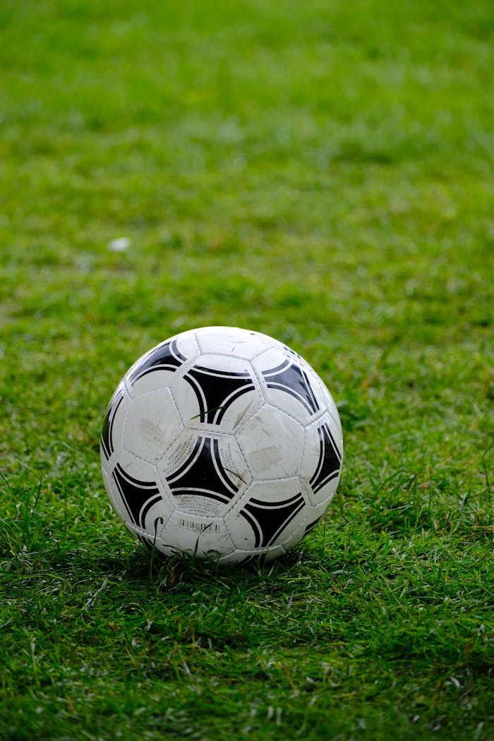 our-story-01 Close-up of a classic soccer ball resting on a lush green field.